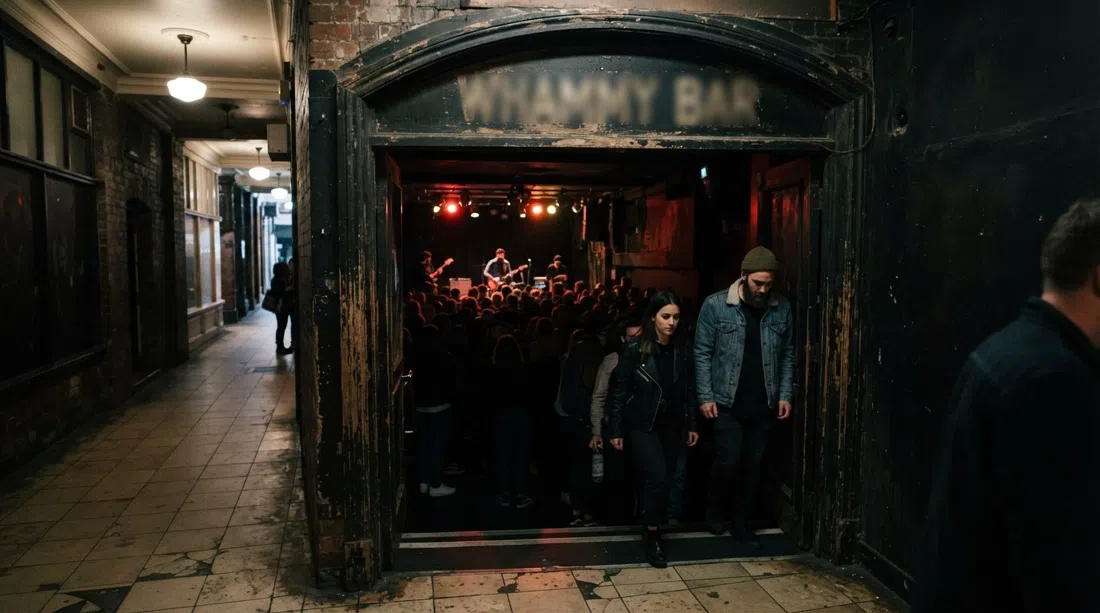 Whammy Bar en St Kevin’s Arcade, iluminación tenue del escenario en el sótano, público oscuro y la estrecha entrada de la galería que insinúa la sala subterránea